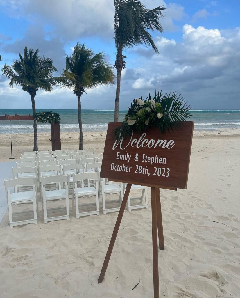 Wood welcome sign with white tropical flowers at a beach wedding ceremony at Secrets Maroma