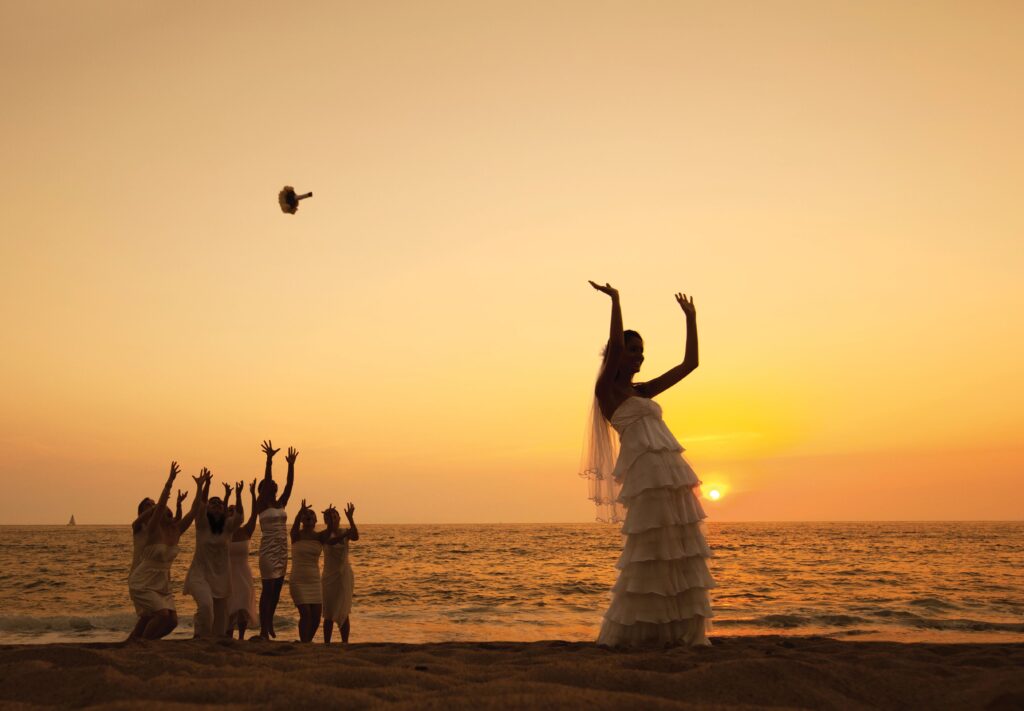 A bride throwing a bouquet at sunset on the beach