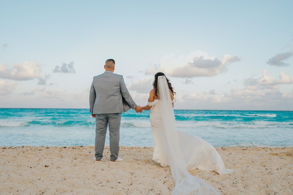 Bride & groom standing on the beach looking out at the ocean