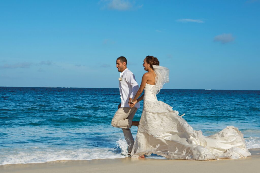 Bride and groom running into the ocean in wedding dress and wedding outfit during destination wedding on the beach
