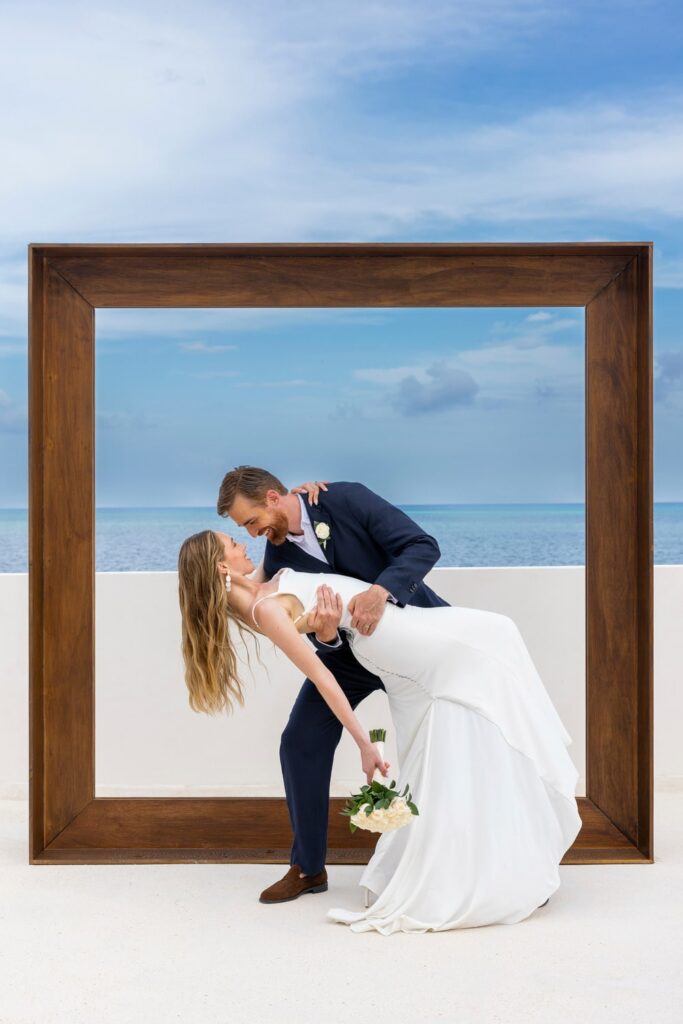 Bride and groom dipping for kiss with the ocean in the back ground