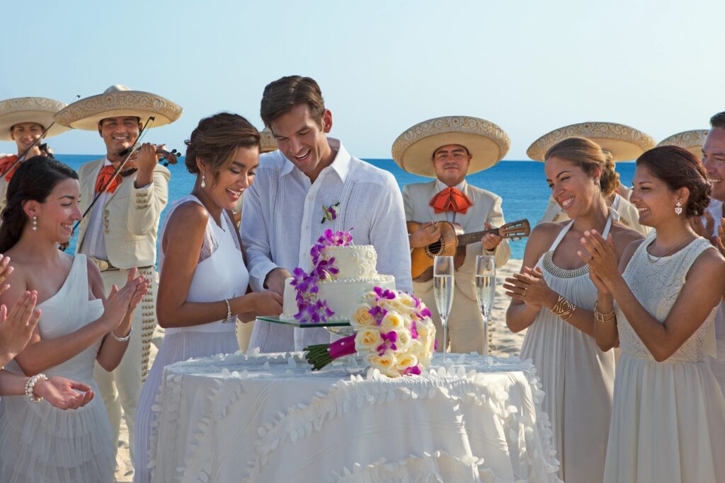 Bride and groom cutting wedding cake with bridesmaids and Mariachi band during destination wedding in Mexico
