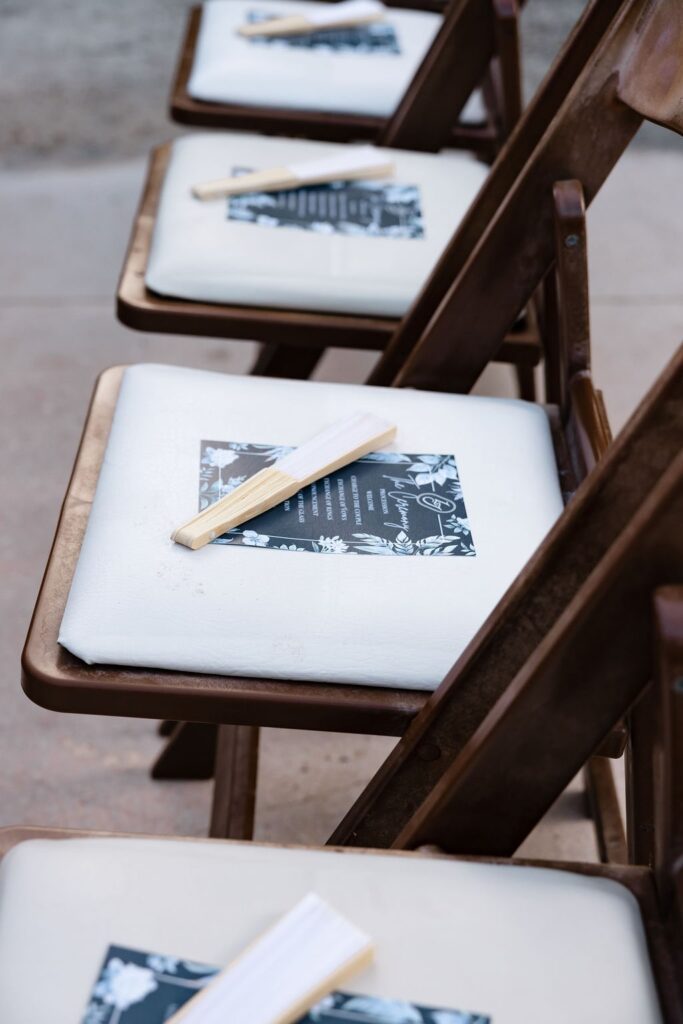 Wedding programs with paper fans on wood chairs at wedding ceremony
