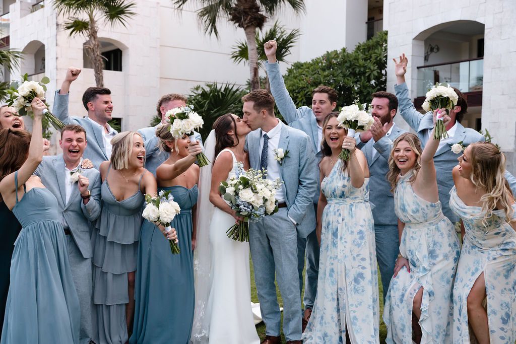 bride and groom kissing surrounded by wedding party in blue and white wedding party outfits