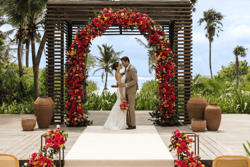 Bride and groom standing under colorful wedding ceremony arch at UNICO 20°87° Hotel Riviera Maya wedding