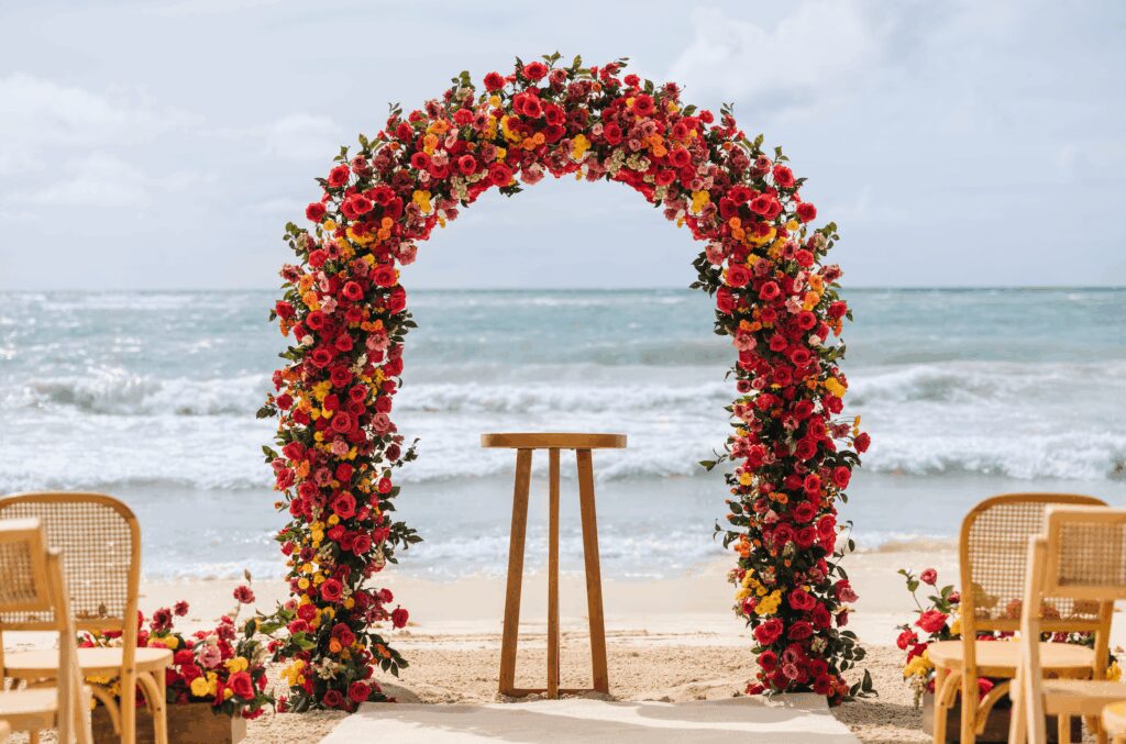 Bright and colorful floral wedding ceremony arch with red and pink flowers at UNICO 20°87° Hotel Riviera Maya wedding on the beach