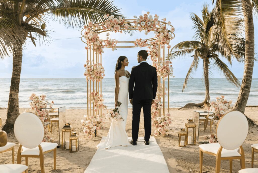 Circular gold wedding ceremony arch with neutral flowers and gold chairs for an elegant beach wedding ceremomy