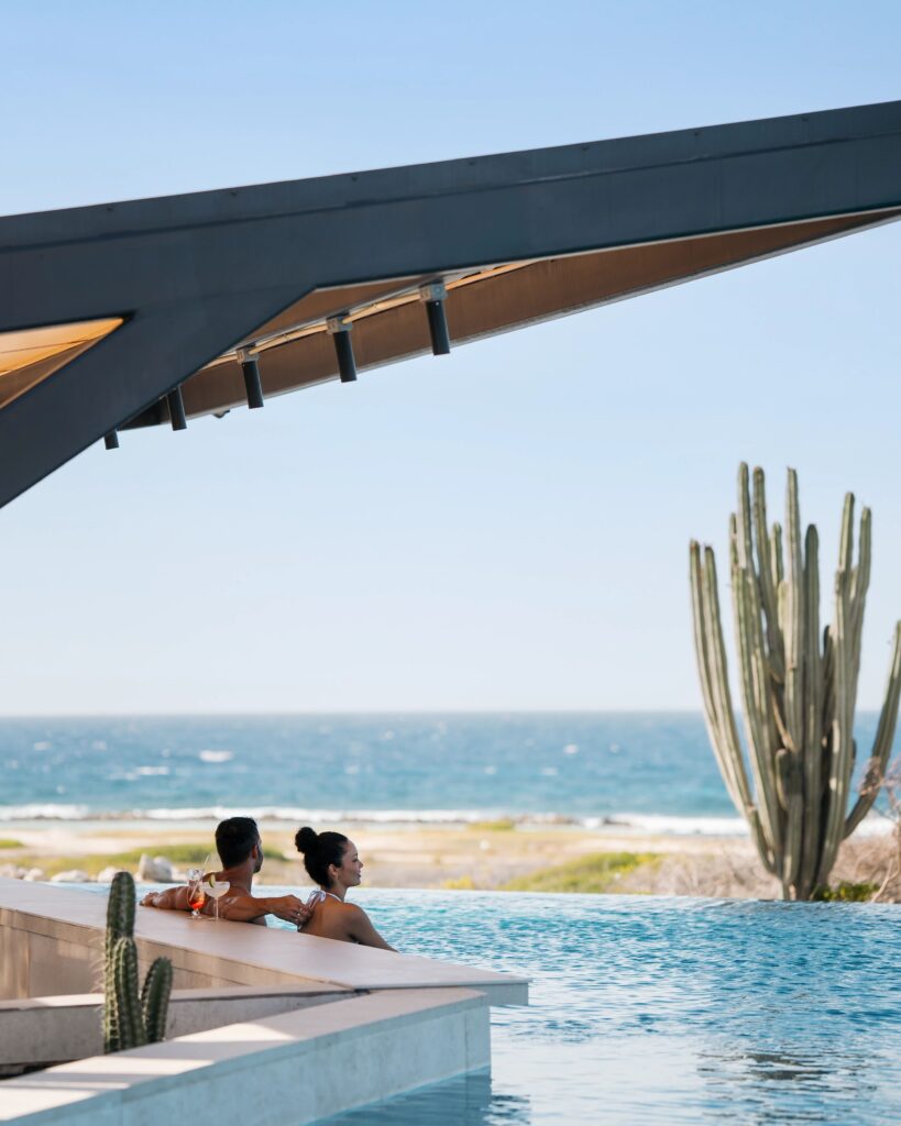 Two adults drinking cocktails by the pool with a view of the Mexico beach at an adults only All-Inclusive resort