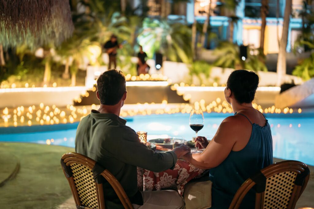 Couple holding hands eating dinner poolside at night