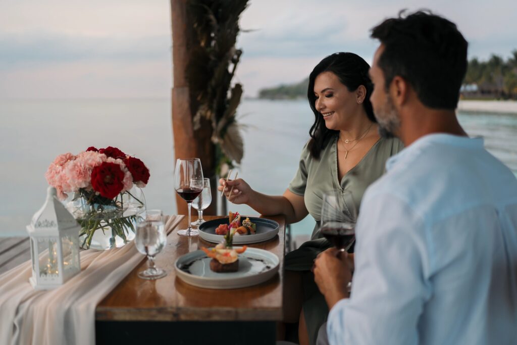 Engaged couple eating dinner at an oceanfront restaurant at sunset