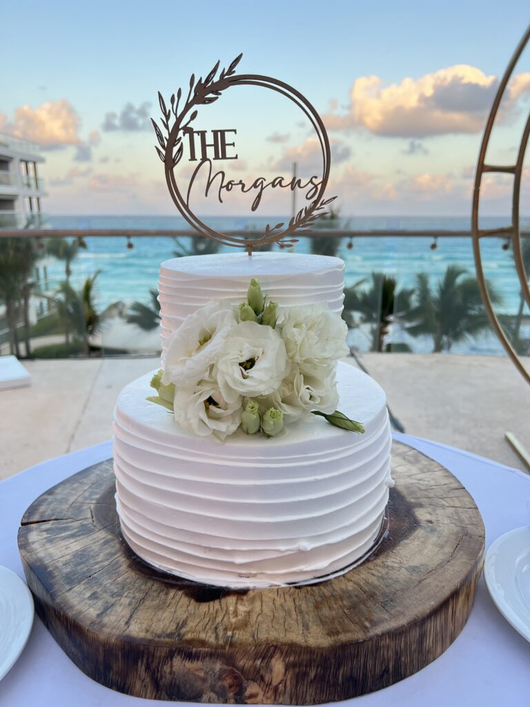 Two tiered buttercream wedding cake with flowers and cake topper at a Cancun wedding