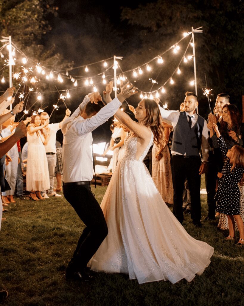 Bride and groom walking through a sparkler send-off at their reception Bride and groom dancing under bistro lights at night